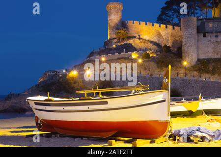 Fishing boat on a sandy beach in the evening against the background of the fortress. Stock Photo
