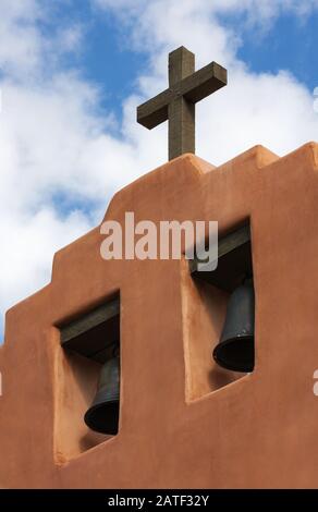 Bells of First Presbyterian Church, adobe stucco church with two bells and wooden crucifix.  Contoured adobe plaster New Mexico USA Stock Photo