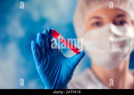 Doctor in medical mask and blue gloves holding tube with blood test. Medicine and health care concept. Stock Photo