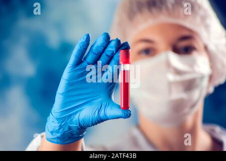 Doctor in medical mask and blue gloves holding tube with blood test. Medicine and health care concept. Stock Photo