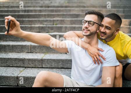 Portrait of happy gay couple spending time together and taking a selfie with mobile phone. Lgbt and love concept. Stock Photo