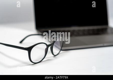 protective glasses on an empty desk with blurred computer screen on background Closeup Stock Photo