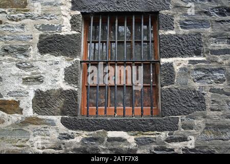 Window with bars and metal grille set in old stone wall, taken at disused whisky warehouse in Scotland. Stock Photo