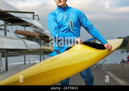 Male athlete in swimming sportswear carrying yellow kayak Stock Photo