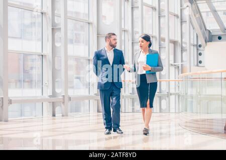 Businessman and businesswoman walk together and talk about business holding coffee in hand Stock Photo