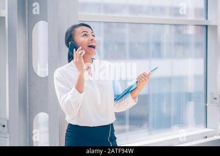 Happy african businesswoman smiling and talking on the phone, holding folder of documents Stock Photo