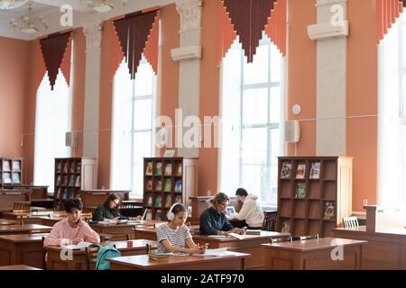 Two rows of desks in college library and students working individually Stock Photo