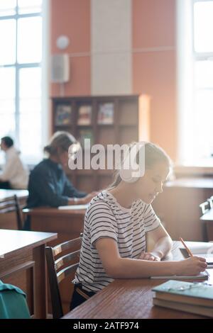 Diligent teenage girl with headphones listening to music and making notes Stock Photo
