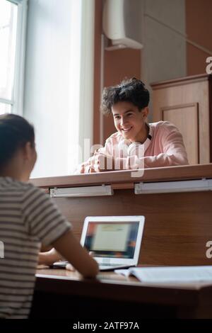 Cheerful handsome guy in casualwear talking to his classmate in library Stock Photo