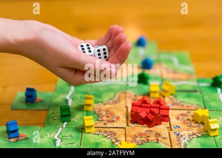 Hand throws the dice on the background of colorful blurred fantasy Board games, gaming moments in dynamics. selected focus. Stock Photo