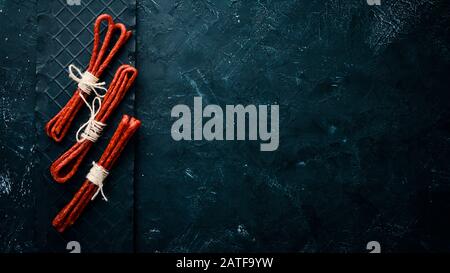 Sausages Kabanosi. On a black stone background. Top view. Free copy space. Stock Photo