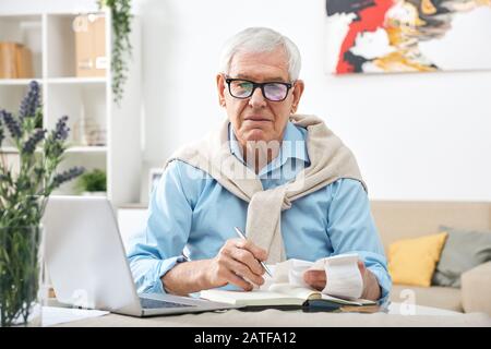 Serious senior man in eyeglasses looking through payment bills by table Stock Photo
