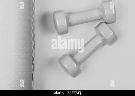 Shaping and fitness equipment. Barbells in small size on yoga mat, close up. Healthy shape and sport concept. Dumbbells made of light green plastic on yellow and purple background, top view Stock Photo