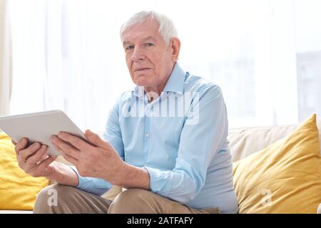 Serious senior man in casualwear looking at you while using digital tablet Stock Photo