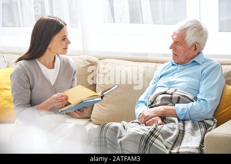 Young female social worker with open book discussing it with senior man Stock Photo