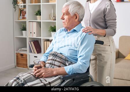 Aged disable man with glass of water sitting on wheelchair Stock Photo