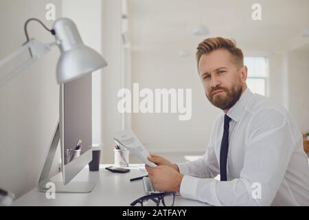 Portrait of a serious busy business man bearded sitting at a table with computers in the office. Stock Photo