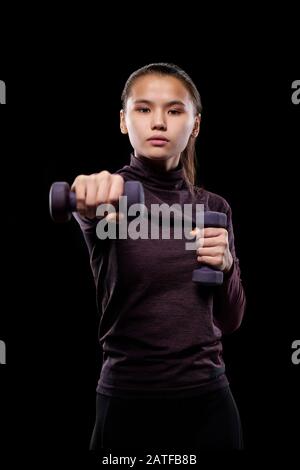 Young active female with dumbbells stretching arm forwards while exercising Stock Photo