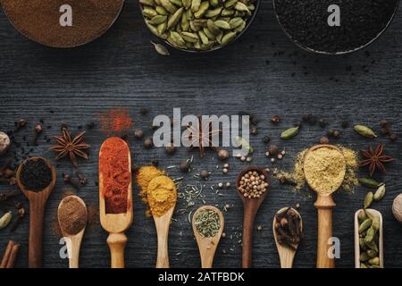 Various aromatic colorful spices and herbs in wooden spoons and scoops. Black ceramic bowls of seasonings. Ingredients for cooking.  Ayurveda treatmen Stock Photo