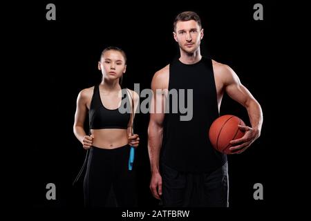 Young sporty couple in black activewear holding skipping-rope and ball Stock Photo