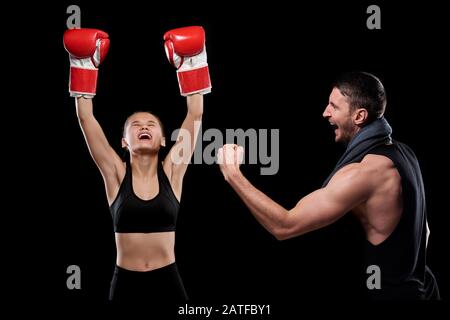 Ecstatic young sportswoman in boxing gloves and her trainer expressing triumph