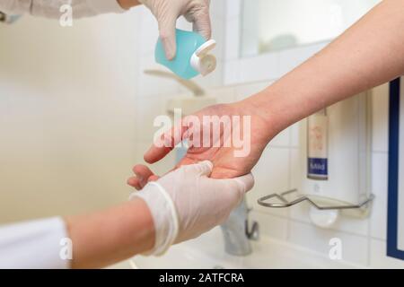 Nurse disinfects a patients hand at a sink Stock Photo