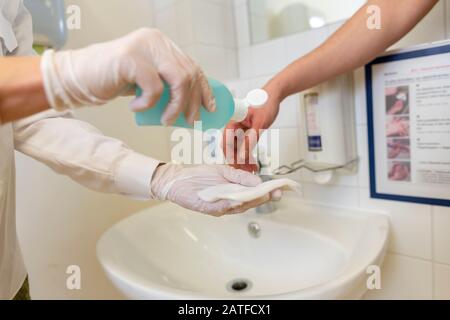 Nurse disinfects a patients hand at a sink Stock Photo