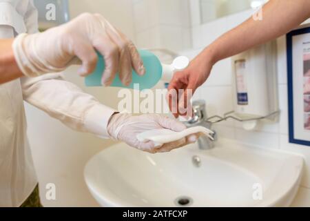 Nurse disinfects a patients hand at a sink Stock Photo