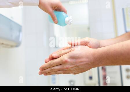 Nurse disinfects a patients hand at a sink Stock Photo