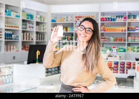 beautiful woman client with smile on her face in pharmacy holding white jar with medicine Stock Photo