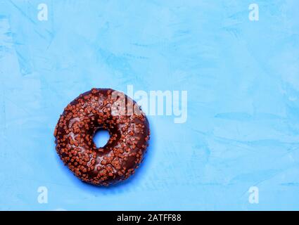 Delicious chocolate donut on a blue concrete surface in cold light. Stock Photo
