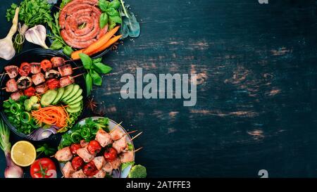 Assortment of baked barbecue meat. Sausages, skewers, fresh vegetables. Tomatoes, onions, garlic. On a wooden background. Copy space. Stock Photo