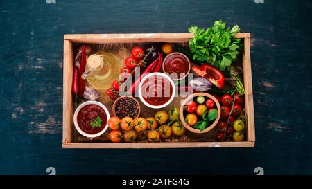 Assortment of tomato sauces in a wooden box. Ketchup. Cherry tomatoes, spices, chili peppers, olive oil, parsley. Top view. Stock Photo