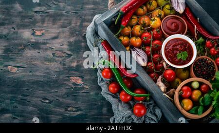 Assortment of tomato sauces in a wooden box. Ketchup. Cherry tomatoes, spices, chili peppers, olive oil, parsley. Top view. Stock Photo