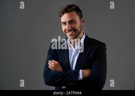 Portrait young smiling businessman. Caucasian guy business suit studio gray background. Modern business person folded his arms over his chest Portrait Stock Photo