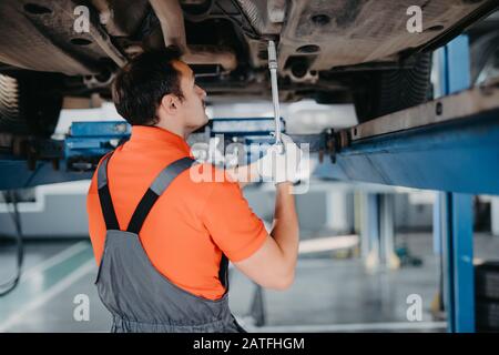 Car service, repair maintenance. Professional car mechanic man working under lifted car in auto repair service. Stock Photo
