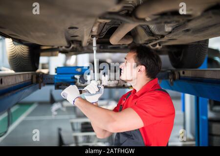 Car service, repair maintenance. Professional car mechanic man working under lifted car in auto repair service. Stock Photo