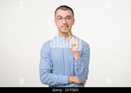 Young hispanic man in glasses is thinking about something with pencil generating idea. Studio shot Stock Photo