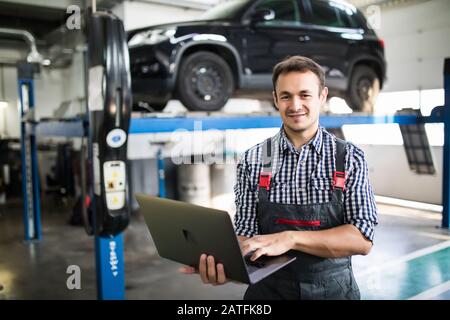 Mechanic using computer diagnostics while repairing car Stock Photo