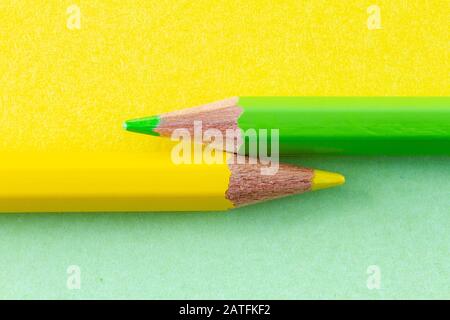 Yellow and green color pencils on yellow and green background color papers arranged horizontally. Minimalist composition. Stock Photo