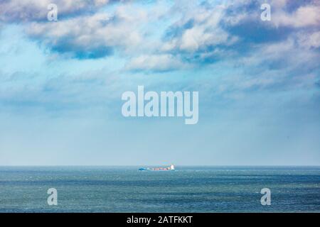 A cargo ship under sunshine and clouds seen in the North Sea from the North Norfolk coastline. Stock Photo