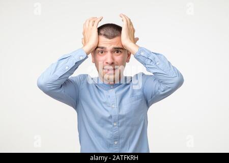 Stressful young hispanic man in blue shirt. Destructive behavior. Studio shot Stock Photo