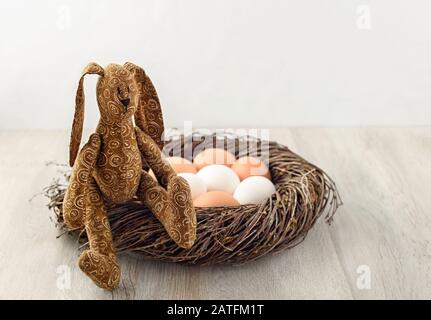 Easter bunny is sitting on a nest on a wooden surface. Stock Photo