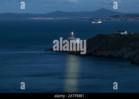 The Baily Lighthouse, Howth. co. Dublin, Baily Lighthouse on Howth cliffs, View of the Baily Lighthouse from the cliff whit cargo ship in background Stock Photo