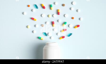 Colorful pills and capsules spilling from a white bottle top view. Creative layout with medical tablets, drug of painkillers, antibiotics, vitamins an Stock Photo