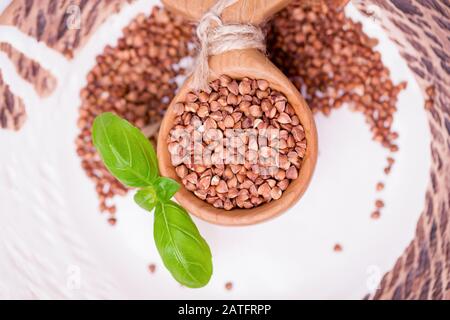 Raw buckwheat groats and basil leaf in wooden spoon on white background, top view. Uncooked buckwheat grains Stock Photo
