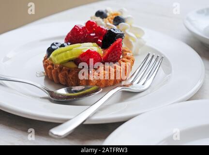 delicious artisanal shortbread fruit cake and whipped cream on white plate with silver fork and spoon, selective focus Stock Photo