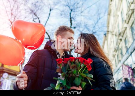 Valentines day date. Man and woman about to kiss outdoors. Couple walking with roses flowers and balloons Stock Photo