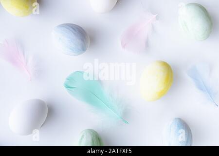 Flat lay of Easter colorful eggs and feathers on white background. Stock Photo
