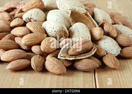 Pile of peeled raw almonds and raw almonds with shells on wooden table. Closeup Stock Photo